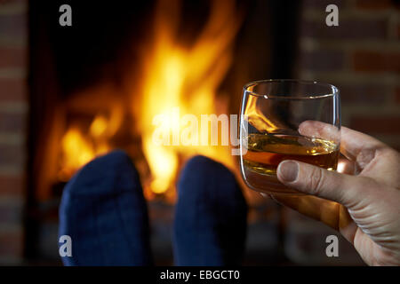 Mann mit Glas Whisky entspannend durch Feuer Stockfoto