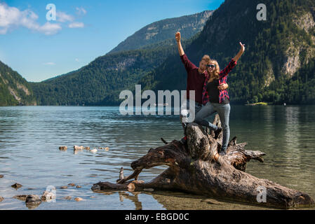 Junges Paar auf einem gefallenen Baumstamm streckte ihre Arme oben in der Luft, Königssee, Nationalpark Berchtesgaden Stockfoto