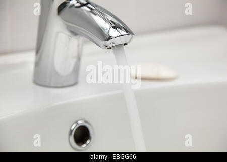 Wasserhahn Wasserhahn mit fließendem Wasser in einem weißen Waschbecken. Stockfoto