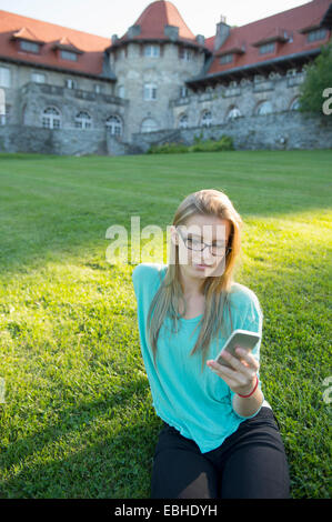 Junge Frau sitzt auf dem Rasen mit smartphone Stockfoto