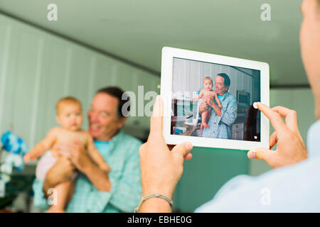 Über Schulter Porträt von Großvater und Baby Enkelin am digital-Tablette im Wohnzimmer Stockfoto