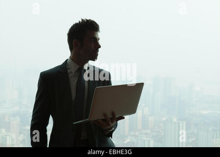 Junger Geschäftsmann mit Laptop vor Wolkenkratzer Bürofenster, Shanghai, China Stockfoto