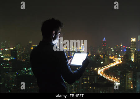 Silhouette junger Geschäftsmann Blick auf digital-Tablette vor Wolkenkratzer Bürofenster in der Nacht, Shanghai, China Stockfoto