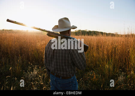 Älterer männlicher Bauer mit Schrotflinte auf der Schulter im Feld in der Abenddämmerung, Plattsburg, Missouri, USA Stockfoto