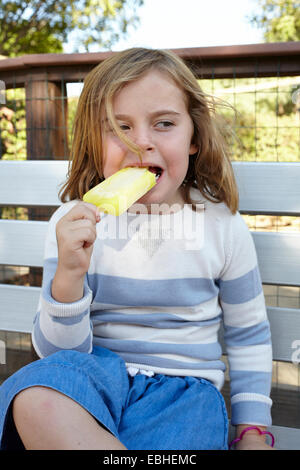 Porträt eines Mädchens essen Eis am Stiel auf Gartenbank Stockfoto