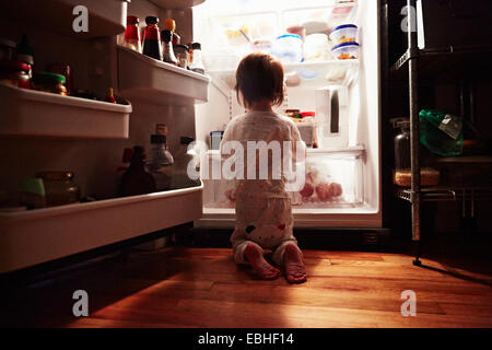 Rückansicht des männlichen Kleinkind kniend vor offenen Kühlschrank in der Nacht Stockfoto
