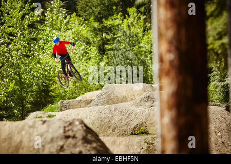 Junge weibliche bmx-Biker springen Luft aus Felsen im Wald Stockfoto