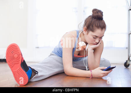 Teenager-Mädchen Aufwärmen und mit Blick auf Smartphone in Ballettschule Stockfoto