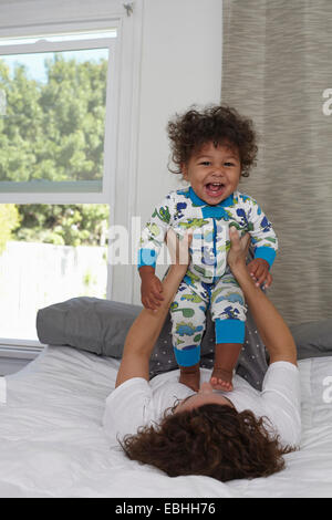 Junge Frau auf Bett Kleinkind Sohn hochhalten Stockfoto