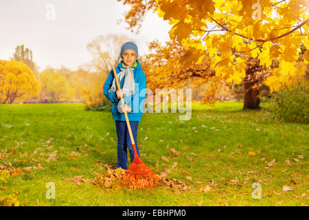 Junge in blauer Jacke mit Harke Rasen Reinigung Stockfoto