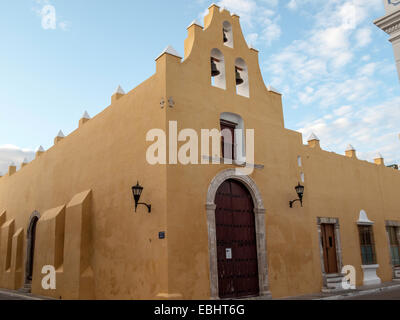 Eckansicht der Kirche Iglesia de San Francisco aus dem 16th. Jahrhundert mit ockerfarbenen Wänden, roter gewölbter Eingangstür, drei Kirchenglocken Campeche, MX. Stockfoto