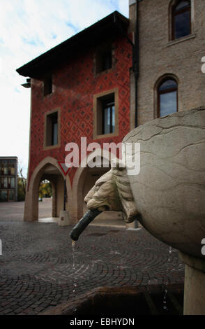 Brunnen mit Löwenkopf vor ein gotisches Gebäude mit voller Fresken verzierte Fassade. Alte Stadt von Pordenone. Italien. Stockfoto