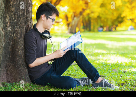Mann Lesebuch im Park, unter einem Baum sitzt. Entspannung im freien lesen. Stockfoto