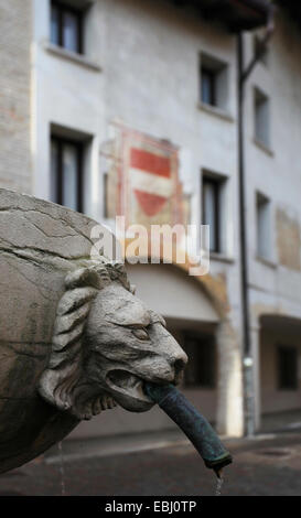 Brunnen mit Löwenkopf vor ein mittelalterliches Gebäude mit Fresko mit dem österreichischen Wappen. Alte Stadt von Pordenone. Stockfoto