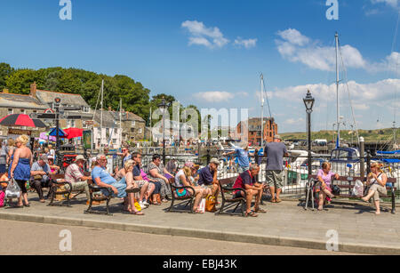 Touristen, die auf Bänken sitzen und die Sommersonne in Padstow Cornwall England Großbritannien genießen Stockfoto