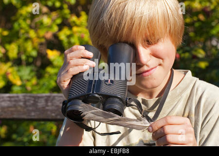 Junge mit einem umgekehrten Fernglases als eine Lupe und schaut auf eine Feder, Deutschland Stockfoto
