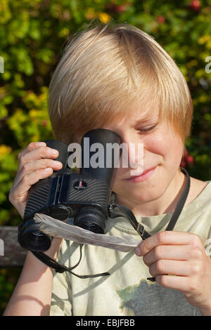 Junge mit einem umgekehrten Fernglases als eine Lupe und schaut auf eine Feder, Deutschland Stockfoto