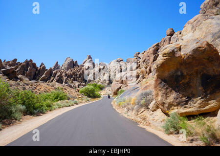 Biker auf einer Landstraße durch die Boulder-ähnliche Felsformationen der Alabama Hills, USA, California, Lone Pine Sanctuary Stockfoto