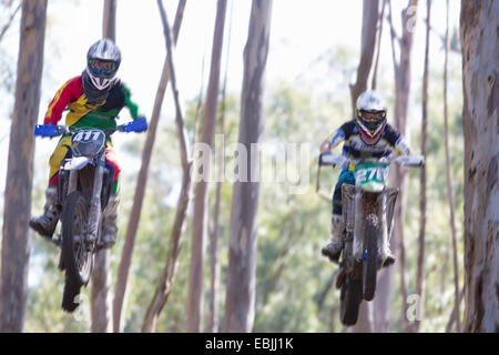 Zwei junge männliche Motocross-Fahrer springen Luft durch Wald Stockfoto