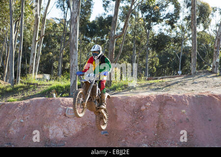 Junge männliche Motocross Racer Schlamm Hügel hinunter springen Stockfoto