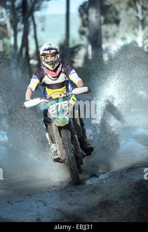 Junge männliche Motocross Racer durch Wald Pfütze planschen Stockfoto