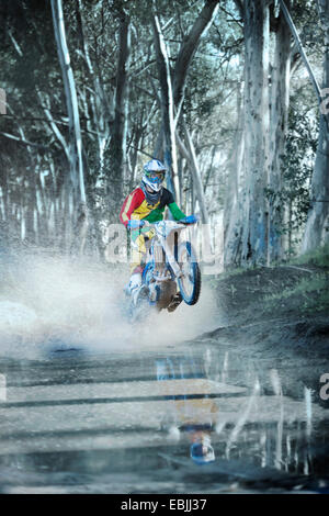 Junge männliche Motocross Racer Reiten durch Feldweg Pfütze im Wald Stockfoto