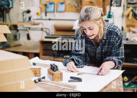 Junge Handwerkerin Messung Blaupause auf Werkbank in Orgel-Werkstatt Stockfoto