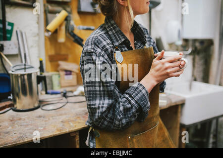 Junge Handwerkerin Kaffeetrinken in Orgel-Werkstatt Stockfoto