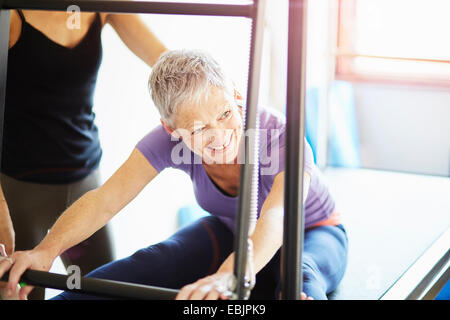 Reife Frau und Tutor praktizieren Pilates auf Trapez-Tisch in Pilates-Fitness-Studio Stockfoto