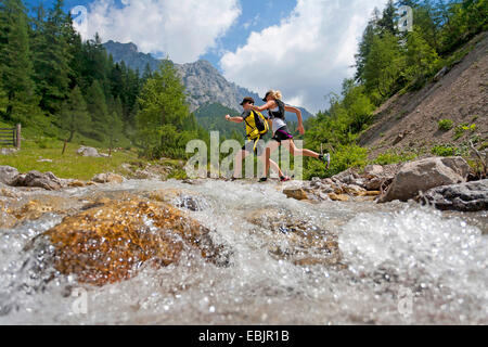 junges Paar, überqueren einen Bach beim Trailrunning im Dachsteingebirge, Österreich, Steiermark, Dachstein Stockfoto