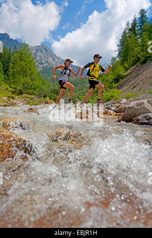 junges Paar, überqueren einen Bach beim Trailrunning im Dachsteingebirge, Österreich, Steiermark, Dachstein Stockfoto