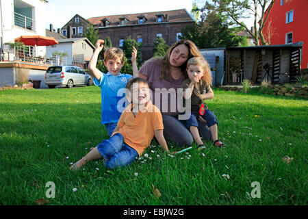 Schwangere Frau mit ihren drei Söhnen auf Rasen im Garten sitzen Stockfoto