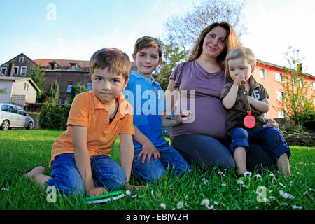 Schwangere Frau mit ihren drei Söhnen auf Rasen im Garten sitzen Stockfoto