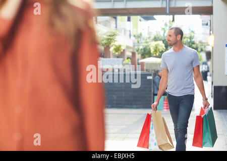 Mitte erwachsenen Mann mit Einkaufstüten, zu Fuß hinter Frau Stockfoto