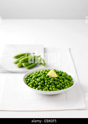 Rohe Erbsenschoten auf Marmor Schneidebrett und Schale gekochte Erbsen mit butter Stockfoto