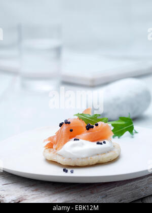 Geräucherter Lachs und Frischkäse Blinis auf Wafer Keks mit Kaviar und Rucola Blätter garnieren Stockfoto