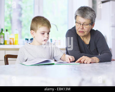 Ältere Frau liest Bilderbuch mit Enkel am Küchentisch Stockfoto