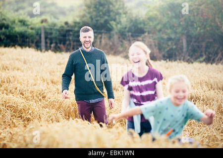 Vater mit zwei Mädchen laufen durch Feld Stockfoto