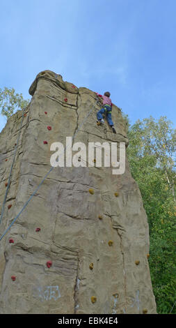 kleiner Junge Klettern angeseilt in eine professionelle Kletterwand Stockfoto