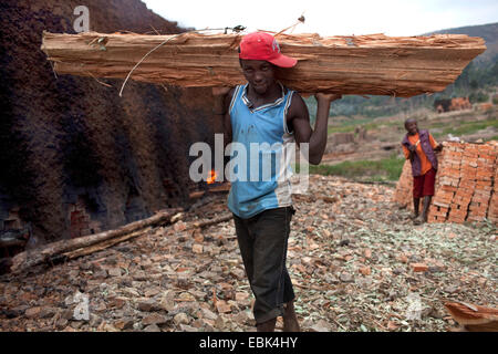 junger Mann mit Holz Balken für das Abfeuern von Ziegelei, Burundi, Karuzi, Buhiga Stockfoto