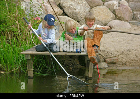 drei Kinder sitzen auf der Promenade, schöpfen und Angeln, Deutschland Stockfoto