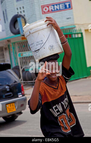 Begrenzung der Schnäbel während des Tragens ein Wassereimer auf seinem Kopf durch starken Verkehr, Bujumbura Burundi, Bujumbura Mairie, junge Stockfoto