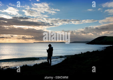 Ein Teenager hört auf seinem iPod beim Betrachten der Aussicht bei Manorbier Bay in der Nähe von Tenby in Pembrokeshire, Wales UK Stockfoto