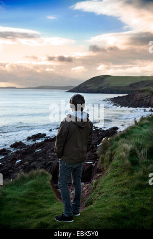 Ein Teenager hört auf seinem iPod beim Betrachten der Aussicht bei Manorbier Bay in der Nähe von Tenby in Pembrokeshire, Wales UK Stockfoto