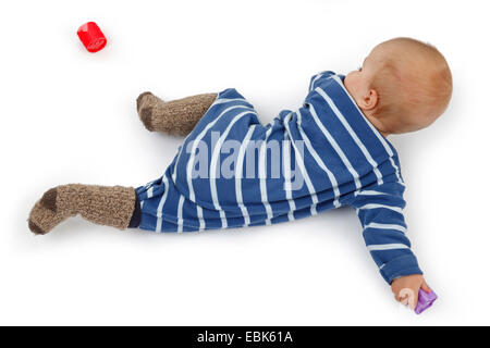 kleines Kind im Strampler auf dem Boden liegend und Suche Babyspielzeug Stockfoto