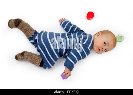 kleines Kind im Strampler auf dem Boden liegen und spielen mit Baby-Spielzeug Stockfoto