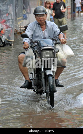 alte Mann reitet auf einem Moped mit vollen Einkaufstüten durch ein Straße überflutet nach ein heftiger Schauer, Thailand, Bangkok Stockfoto