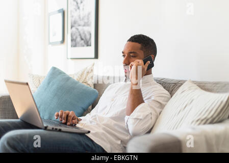 Mann sitzt im Wohnzimmer, mit Laptop und Handy Stockfoto