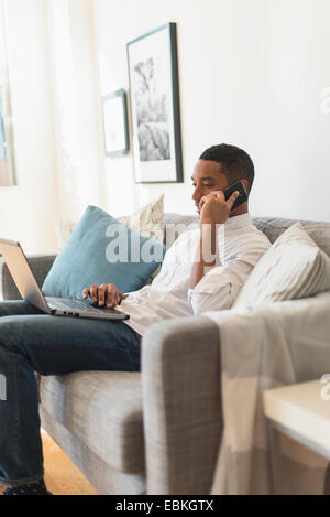 Mann sitzt im Wohnzimmer, mit Laptop und Handy Stockfoto