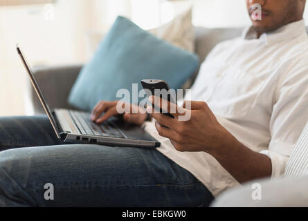 Mann sitzt im Wohnzimmer, mit Laptop und Handy Stockfoto